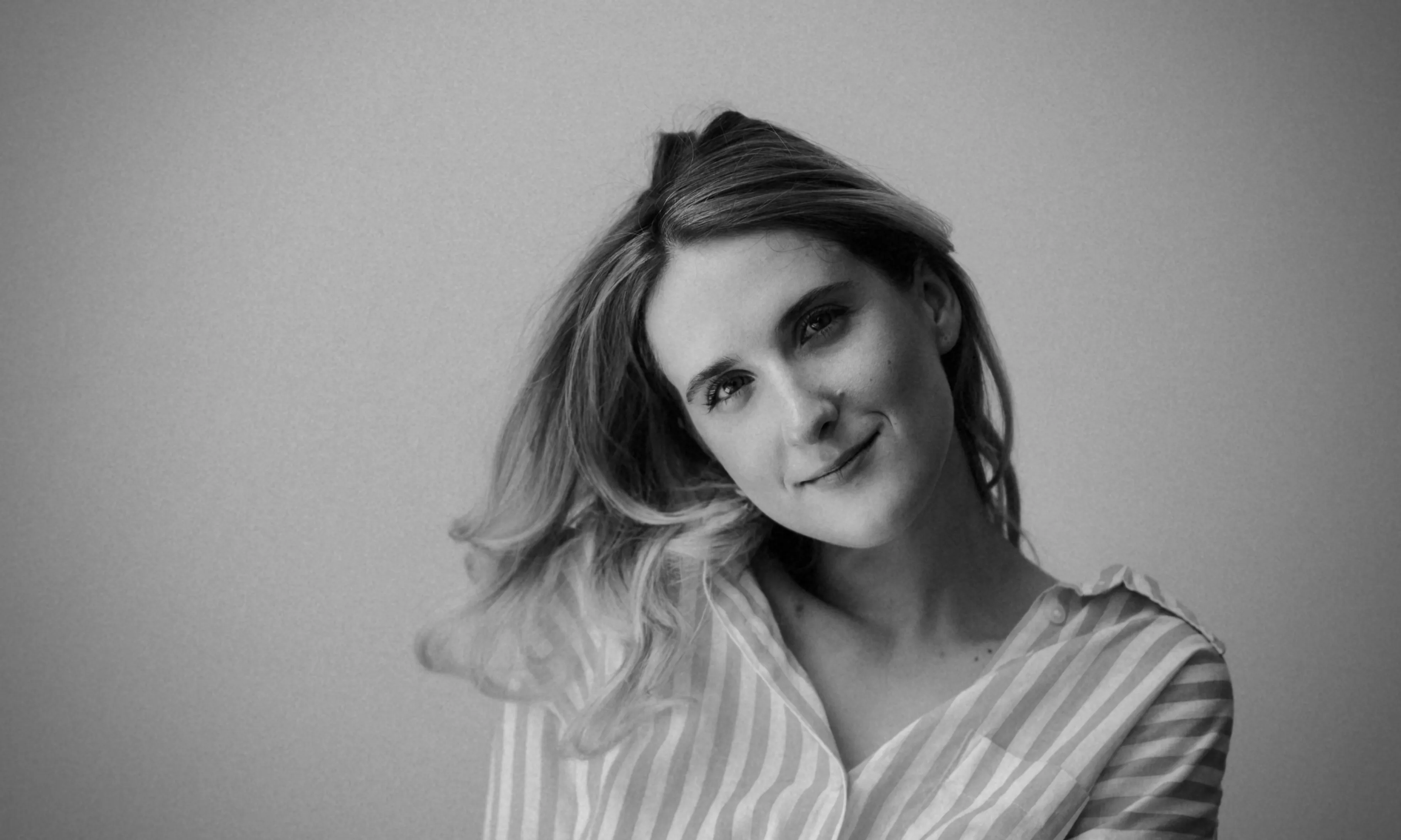 A black and white close up of a woman in a striped shirt, smiling, looking directly at the camera